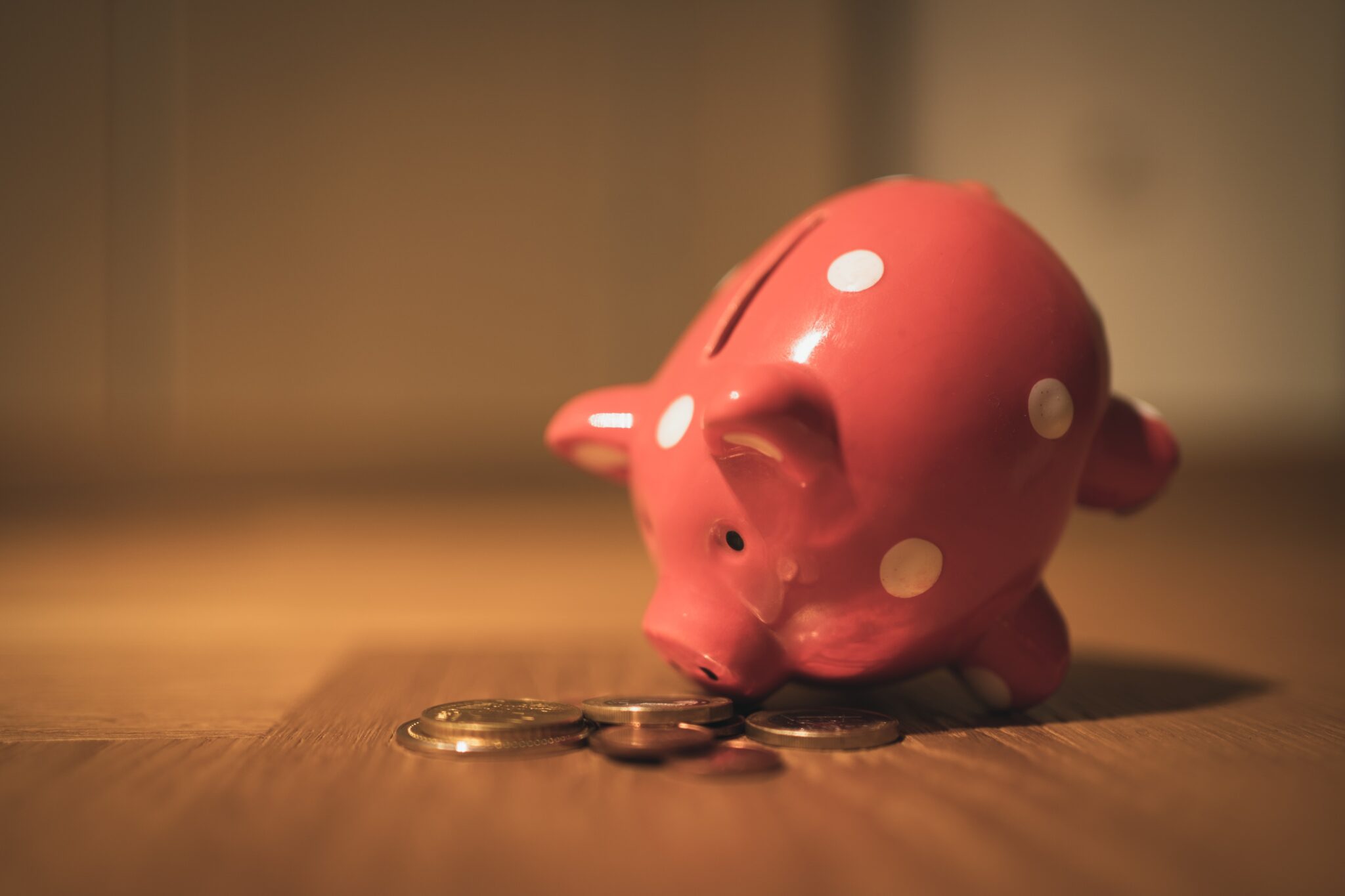Red piggy bank leaning forward with coins in front of it