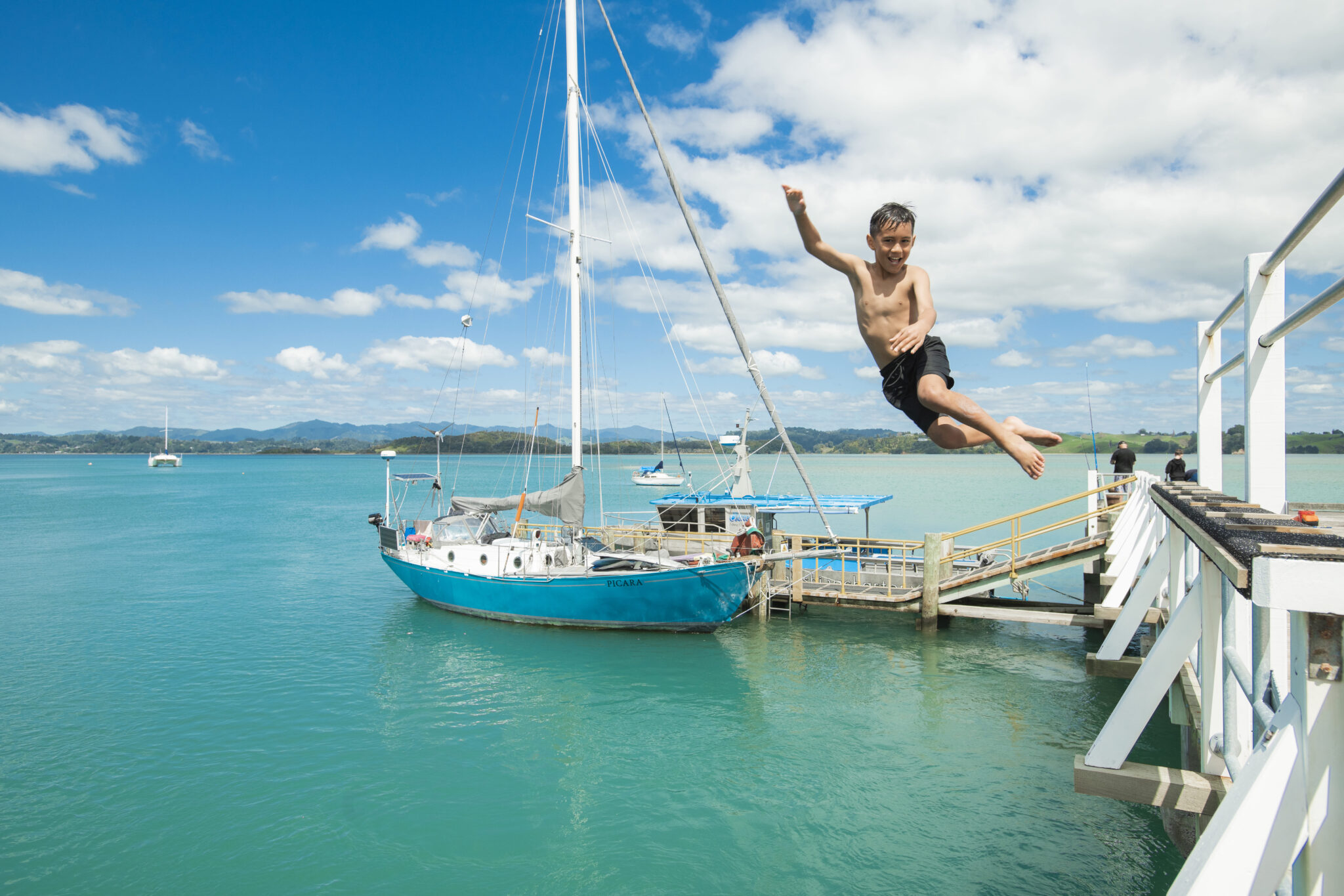 Wharf jumping with sail boat in background